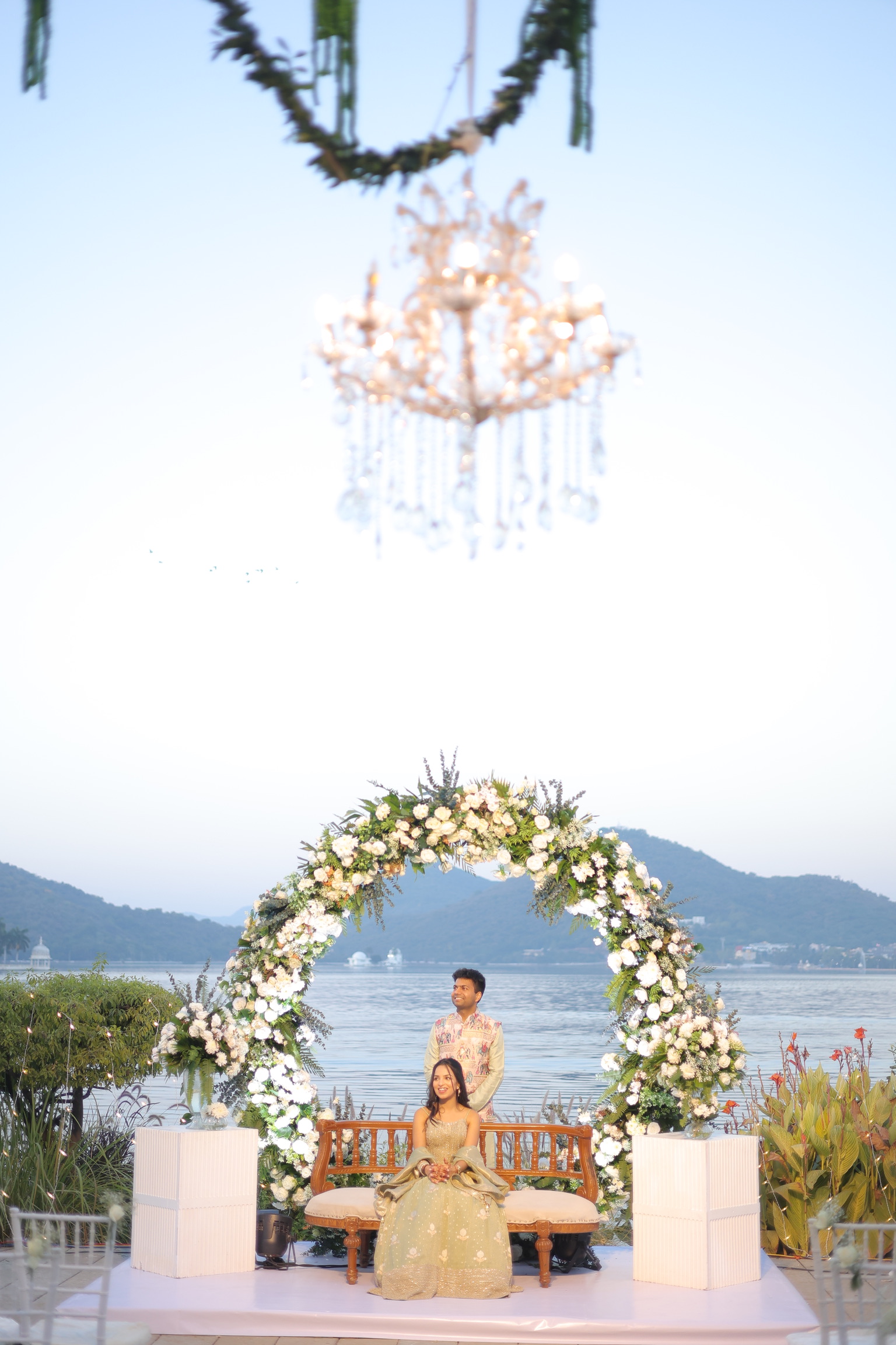 The couple beneath a floral arch by the lake in Udaipur